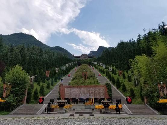 a photo of a grand staicase, massive, going up the mountain, rows of pine trees bookending it, at the top is a massive head of shennong, his big oxen hons coming form his head, the sky is blue with white clouds