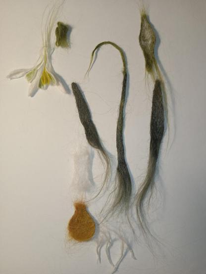 On a white background lie parts of the craft, made from nettles using needle felting. This will be a bookmark in the form of a snowdrop. Thank you for your attention!