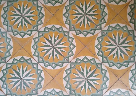 A photograph of decorated square floor tiles. The main motif is a 16-pointed star inside two interlaced eight-pointed stars. The main colours are white, green, light green and yellow.