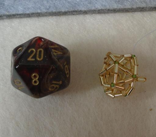 On the left, a d20 die, which is a perfect icosahedron.  It is dark red, marbled, with the numbers inked in gold

On the right, a smaller thing made from beads which is an extremely imperfect icosahedron.  There are tiny green seed beads at the vertices, and each edge is made from two gold bugle beads strung end to end.  There are about two decent triangles in the whole shape; the rest have bent in various places so it looks extremely wonky.