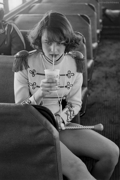 assise dans un bus, une majorette en tenue sirote à la paille une boisson sucrée
