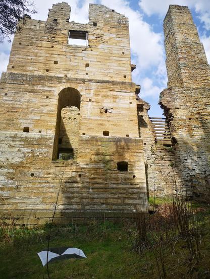 The ruin of Shildon Engine House. A main sandstone tower about 15m high has a tall arched opening in one wall. There is another window and many post holes. To the right is a square chimney of same height. A drone can be seen centre right of the tower.