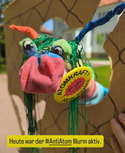 Der Wurm. Eine Bunte Socke mit Augen und Antennen. Sie guckt durch Zaun mit Loch aus Pappe