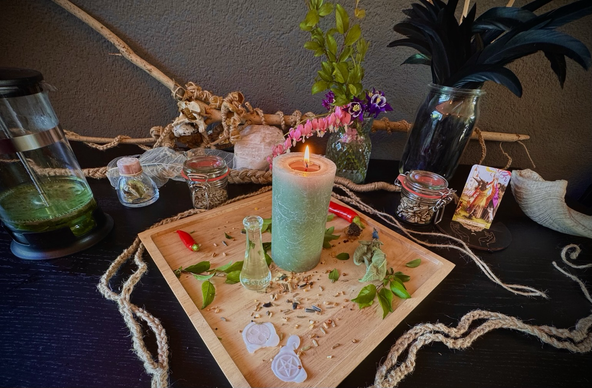 Beltane inspired altar. Loads of plants, seeds, braids, feathers, and a green candle in the middle.