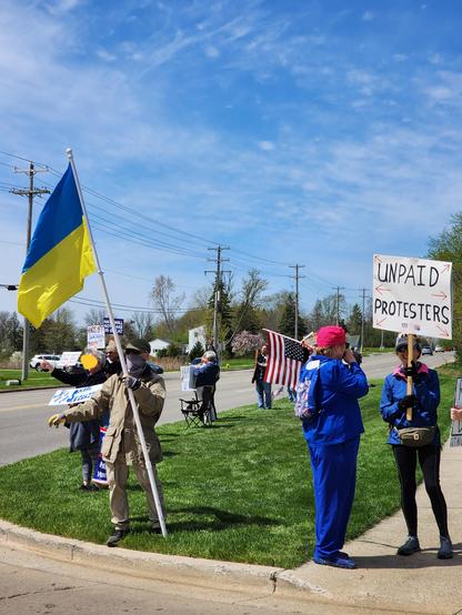 Ukranian flag in foreground; several brightly colored clothing-wearing folks protesting.