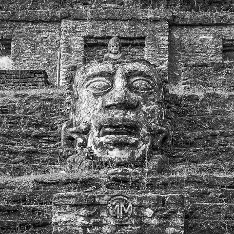 A stone statue of a face on stone steps in black and white