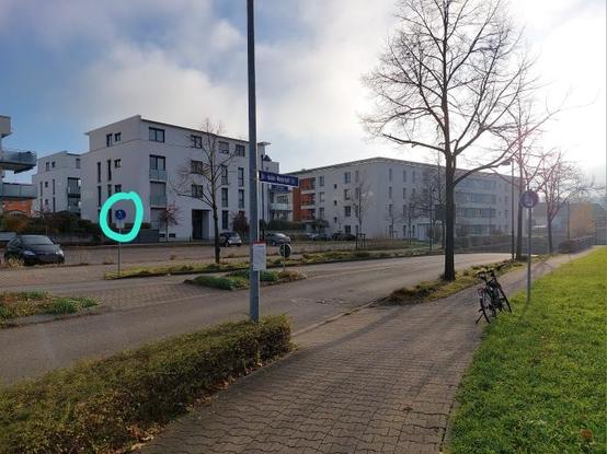 Blick vom westlichen Quadranten des Kreisverkehrs über die Dr.-Isidor-Meyerhoff-Straße hinweg. Auf der anderen Straßenseite steht ein Verkehrszeichen 240. Zum Befahren der Furt, die über keine Furtmarkierung verfügt, muss man einen scharfen 90°-Knick fahren.