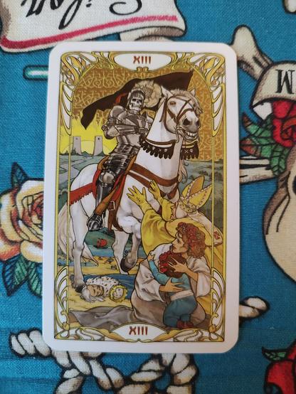 Card from the Golden Art Nouveau Tarot deck. 
Death-XIII.
Death riding a white horse, a skeleton wearing armor. A bishop and a woman with a child cower in fear.