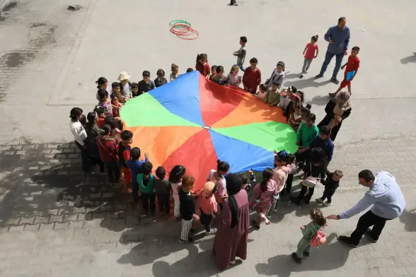 Children stand around a multicoloured circle.