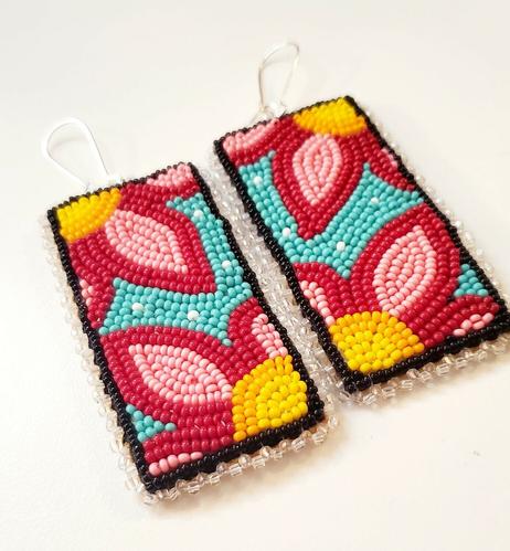 a pair of beaded panels by kiamichi as dangling earrings depicting flowers in pink and yellow on a teal background