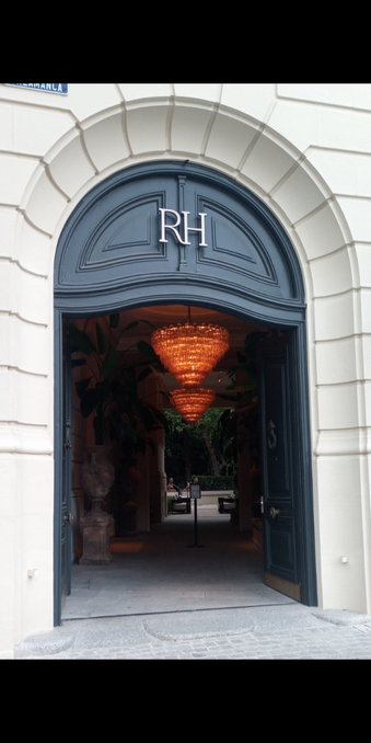 On open doorway with two warmlynlit chandeliers and a green leafed garden through a second dooway