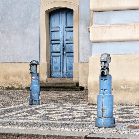 Metal sculptures with futuristic heads in front of a blue door in Prague.