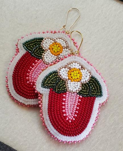 a pair of beaded earrings made by kiamichi representing halved strawberries in red and pink with their white and yellow flowers and green leaves on top