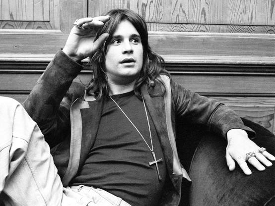 A young John Michael Osbourne sitting in a chair, relaxed pose, crucifix around his neck. Animated looking to the right away from the camera. 

source https://en.wikipedia.org/wiki/Ozzy_Osbourne