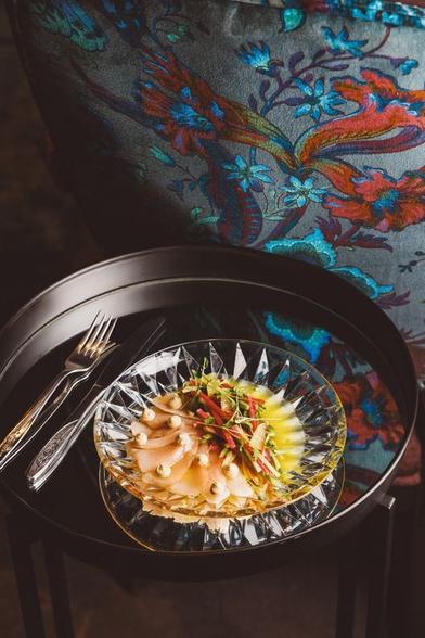 A beautiful plate of food on a small table next to a sofa upholstered in jewel toned paisley.
