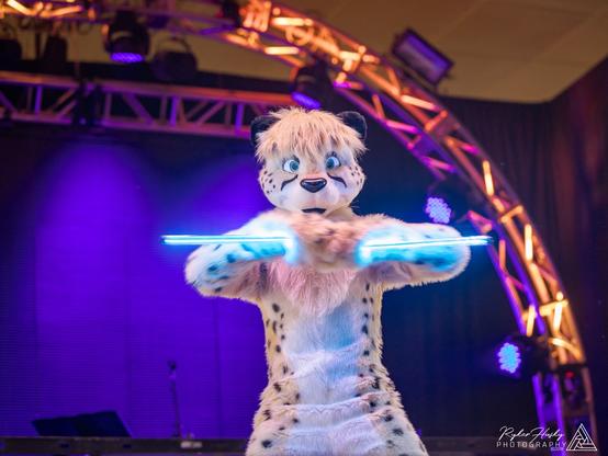 Shadow Cheetah on stage in BLFC dance competition. The picture catches a moment with an overly dramatic pose, and the two glowsticks look like the galaxy's teeny tiniest light sabers.