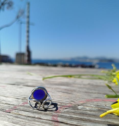 the inner side of a silver open ring with a big blue stone, it's placed on wooden floor with blue sky in the background