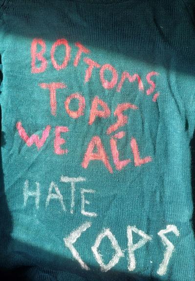 Bottoms, Tops, We All Hate Cops. Painted raggedly on a turquoise top.