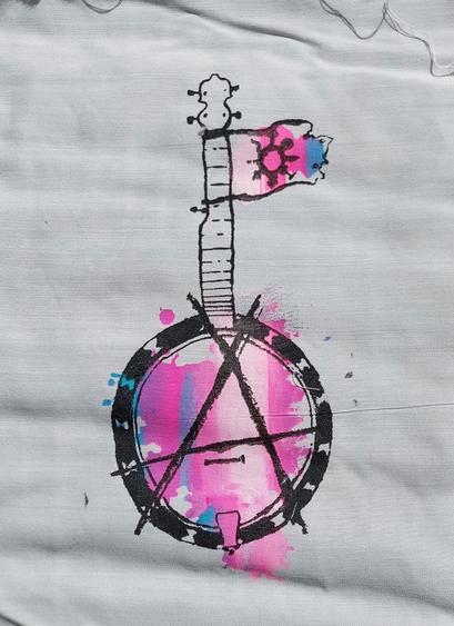 A screenprinted drawing of a banjo. Near the head, there is a small flag with a gender chaos symbol attached. Over the other head, the banjo head, there is an a drawn in such a way to make a circle A together with the instruments' shape.