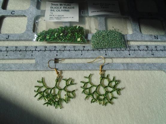 Another pair of the doubling-up bugle bead earrings as posted yesterday, but this pair is in olive green, so it shows up more clearly against the background.  The beads used to make them are also shown; they are Miyuki 3 mm bugle beads in silver-lined olivine, and Miyuki 15/0 seed beads in basically the same colour.  There's also a 3 mm Czech firepolish bead at the top of each earring again, and, once again, it's a very good match for the rest of the beads.

I don't plan to make them all self-coloured.  There will be some involving contrasts.