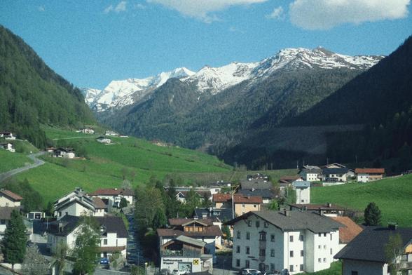 Snow covered Alps alongside Brenner railway while the valley is lush and green.