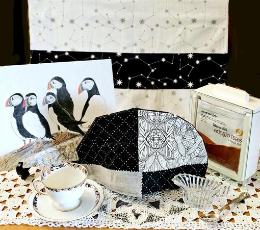 Black and white tea tableau featuring constellations of stars and a pen drawing of puffins, plus a handmade cozt, vintage china, vintage glass, and Decaf Earl Grey black tea from Adagio.