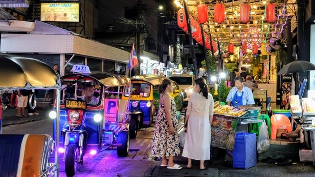 color photo taken at night of a busy night market where a line of tuktuk waiting for customers along a busy street next to a seafood restaurant.