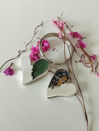 two silver hearts, in the one is visible a pcb and in the other wristwatch' elements. Also there are and pink small flowers in the scene
