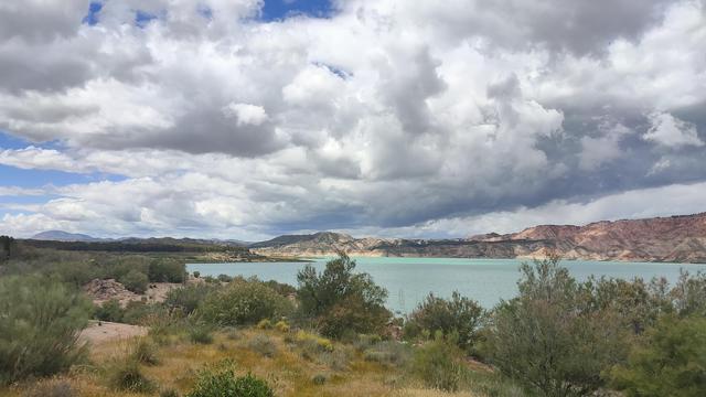 Wide shot of a huge lake, aqua blue water. Lots of white fluffy clouds rolling in