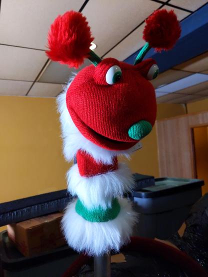 A brightly colored red, white, and green puppet with antennas, bulging eyes, and a big mouth. It would be horrifying if it weren't so cartoonishly cute.