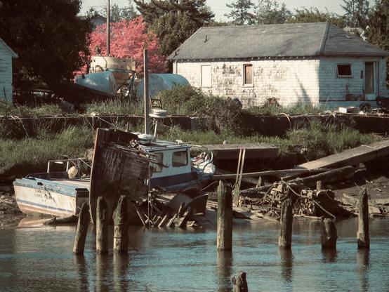 Old broken down boat on a river in front of an old broken down house