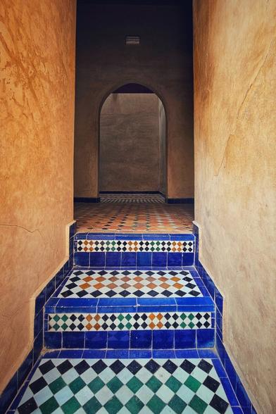 A view looking up a short set of stairs with colorful geometric tile patterns, leading to an arched doorway and tiled floor in a building with textured beige walls.