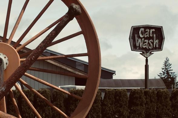 A spoked nautical wheel in foreground, a retro car wash sign in the background.