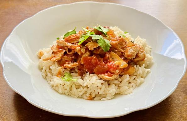 Chicken Tinga on rice, in a white soup plate with scalloped edges. Cilantro as garnish.