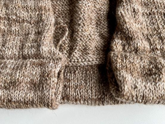 Knitted fabric in shades of brown and cream with a folded hem show on the outside and the inside in the gap in the middle. On the wrong side you can see the tiny braid at the 'seam' as a result of the three needle bind off.