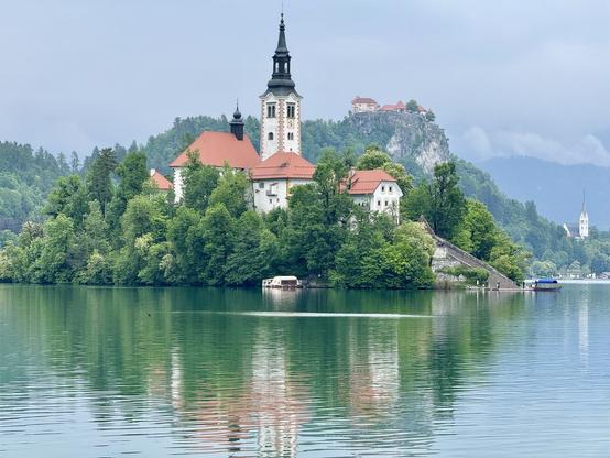 Bled Castle rises behind Bled Island; a church steeple is seen right of frame