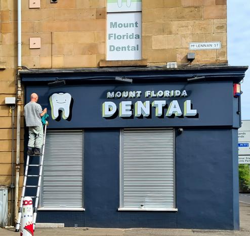 A sign writer putting the finishing touches to a hand-painted shop sign.