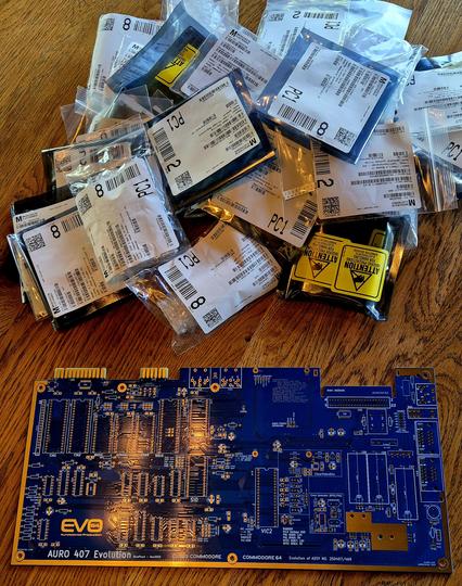A nice, bare blue pcb for a Commodore 64 in the foreground, with a heap of bags with components in the background.