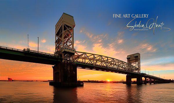 The Cape Fear Memorial Bridge at Wilmington, North Carolina is shown here with a stunning display of colors at sunset. The sunset behind the bridge shows glorious colors of yellow and gold in the deep blue sky. From the Fine Art Gallery of Shelia Hunt.