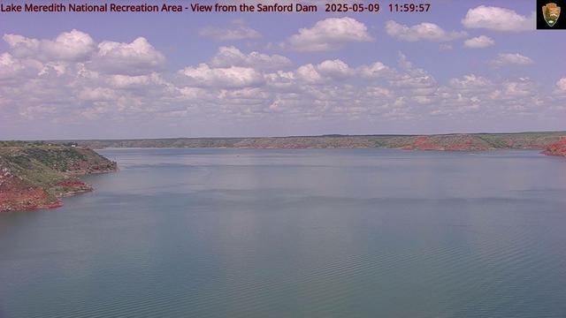 The Sanford Dam holds back the Canadian River in this National Park Service web camera view from Lake Meredith National Recreation Area. The sky today is especially beautiful-gentle blue in color with a collection of white-topped, grey-bottomed clouds. The clouds may be cumulus-fluffy, white, similar to a cotton ball. The landscape surrounding the reservoir shows off red soils and green vegetation.