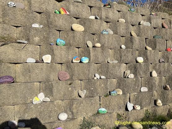 A photograph of lines of pebbles along a beach wall, many of which have been painted.