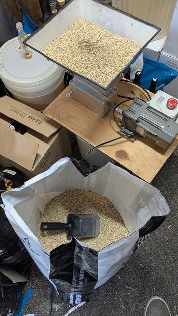 A sack of pale malt next to a mill that is crushing said malt, the hopper of the mill is fairly full.