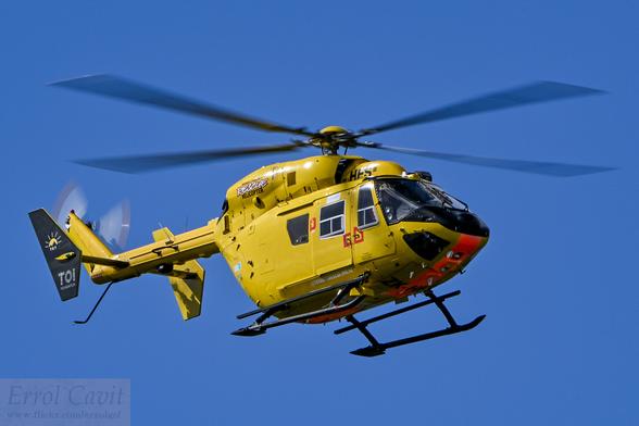 Yellow rescue helicopter from below and front quarter, which blue sky behind.