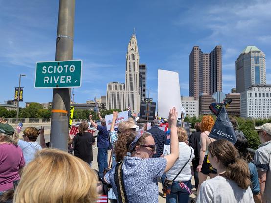 A crowd of people at a downtown bridge holding protest signs.