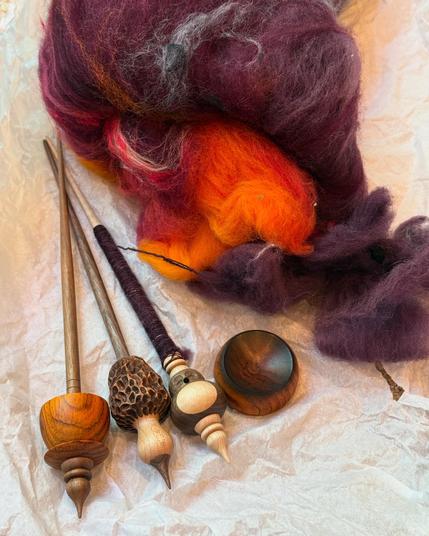 Top and center: batt of fiber in colors ranging from purplish brown to orange. Lower left, 3 supported spindles - one teacup style, one morel mushroom, one owl. Owl spindle has in progress cop. Also shown spinning bowl