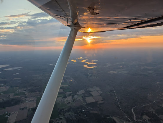 The sun setting somewhere over Northern Wisconsin as seen from a small airplane. The sky has a burnt orange hue with the haze.