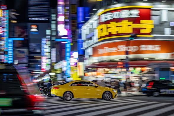 Panning shot of a yellow sport car speeding on a busy street at night in Shinjuku, Tokyo, Japan, on a background of skyscrappers illuminated by neon lighting.
