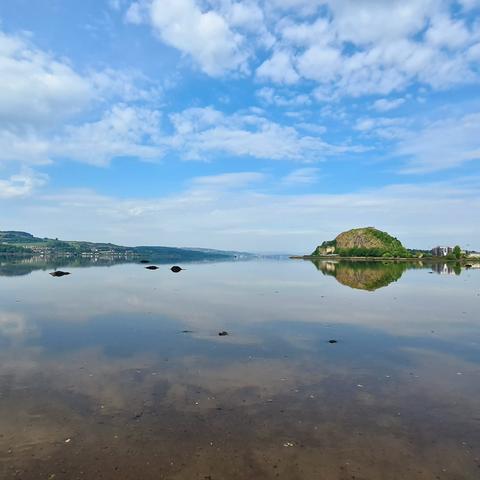 The Clyde reflected in still waters, with a large hill, consisting of the exposed plug of an extinct volcano, visible in the distance.
.