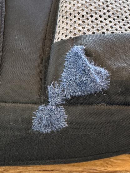 The picture shows the bottom of a black backpack. There are patches in blue yarn.