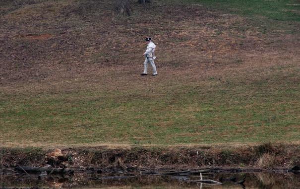 A man dressed as an American Revolutionary War soldier walks down a hill and by a creek alone.